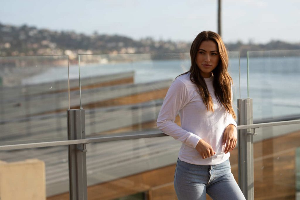  a girl in a long-sleeved t-shirt stands leaning against a glass railing