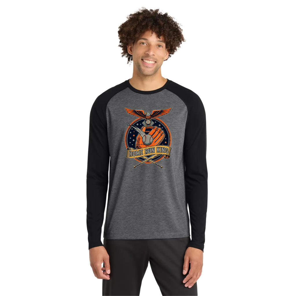A man wearing a Tri Blend Two Tone Raglan LS Tee in gray and black color with a graphic design featuring an eagle, a baseball glove, and the text "Home Run King" in vibrant colors.


